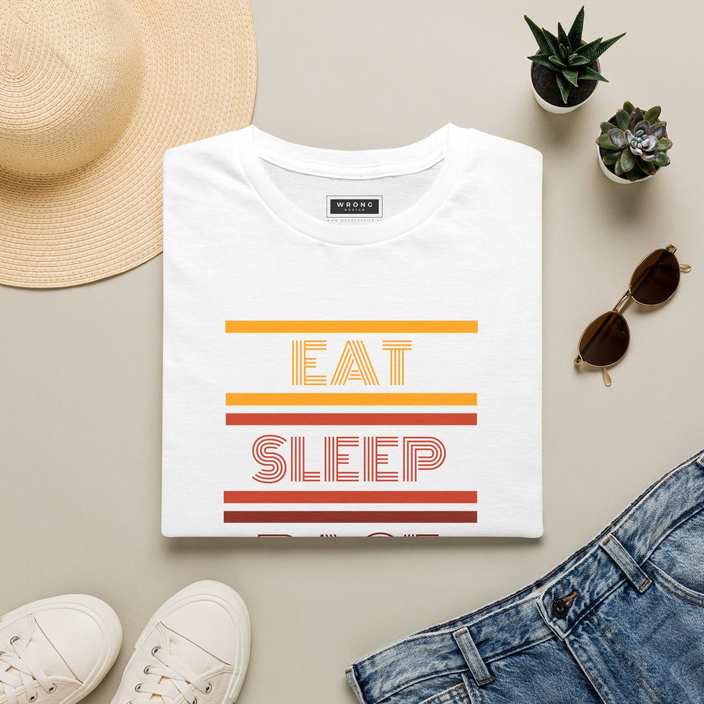 A folded white graphic T-shirt with retro orange and red stripes and the words 'EAT SLEEP' is styled in a flat lay with a straw hat, white sneakers, sunglasses, small potted succulents, and blue jeans on a light beige background.